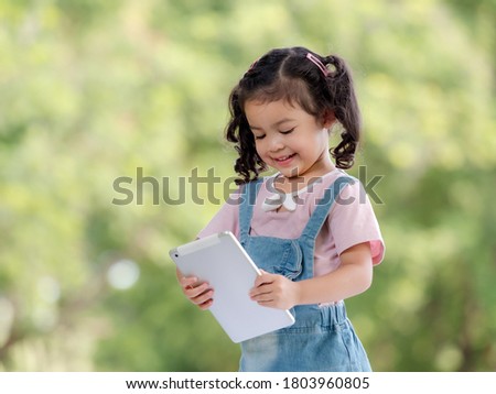 A cute Asian girl is using a tablet for fun playing games and learning outside of school in the park