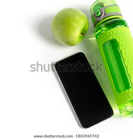 Green fitness bottle. apple and black mobile phone mock up laying near with light leak in the corner. Training application concept. Square format image.