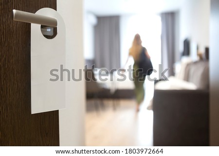 Privacy sign hanging on handle of open door to hotel room with standing person. Copy space.