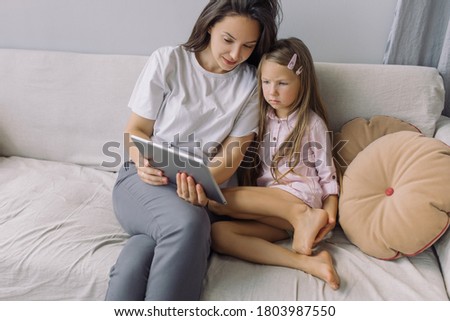 Young beautiful mother showing educational cartoon on tablet to her little daughter. Family time.