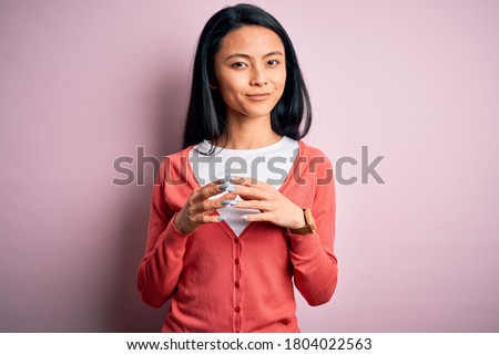 Young beautiful chinese woman wearing casual sweater over isolated pink background Hands together and fingers crossed smiling relaxed and cheerful. Success and optimistic