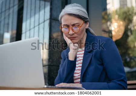 Tired asian businesswoman working project, using laptop, searching information, brainstorming. Portrait of frustrated mature woman sitting at workplace 