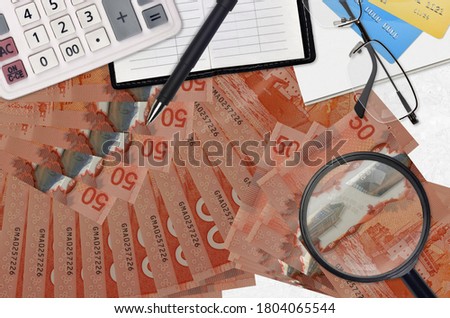 50 Canadian dollars bills and calculator with glasses and pen. Tax payment season concept or investment solutions. Searching a job with high salary