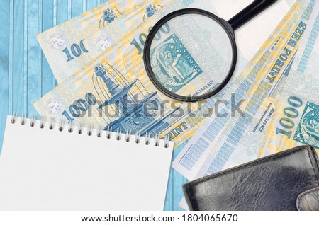 1000 Hungarian forint bills and magnifying glass with black purse and notepad. Concept of counterfeit money. Search for differences in details on money bills to detect fake
