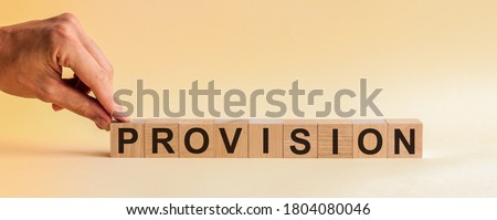 The hand puts a wooden cube with the letter P from the word PROVISION. The word is written on wooden cubes standing on the yellow surface of the table. Concept. Royalty-Free Stock Photo #1804080046