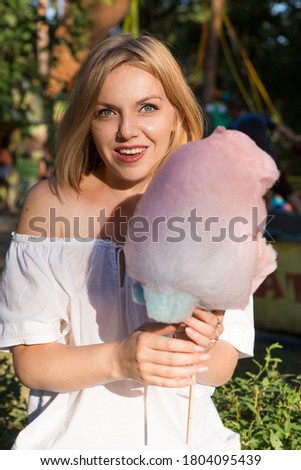 Smiling young woman eating cotton candy at amusement park	
