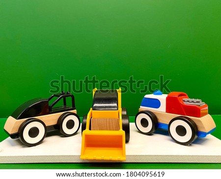 three multi-colored toy cars made of eco-friendly wood and plastic, on a green solid background