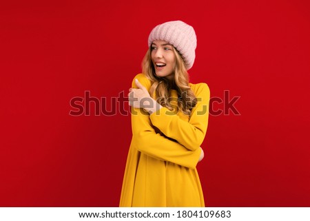 Happy beautiful young woman in a warm hat on her head, on a red background, autumn concept