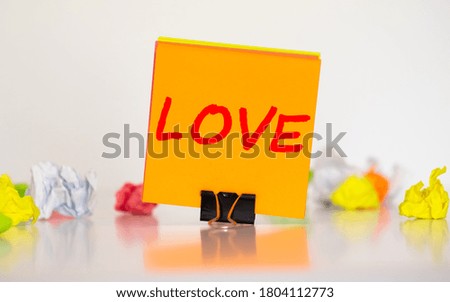 Pink sticky note with written word LOVE on a wooden background.