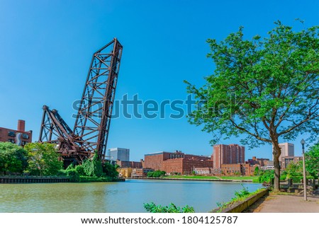 Cuyahoga River runs by a raised draw bridge and through the town of Cleveland, Ohio. Parks and brick buildings line both sides of the water.