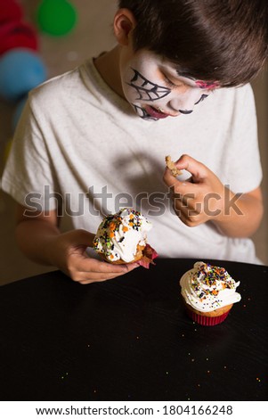 Boy with a face paint eating spooky Halloween cupcakes