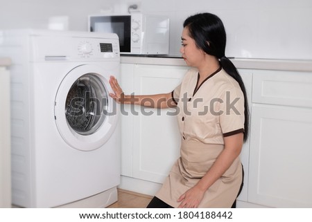 Young beautiful Asia maid loading the washing machine clothing in hotel room