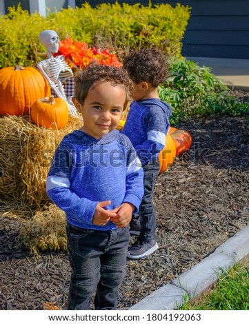 African-American twin toddlers playing in front of their house with Halloween decorations; one tween looking at camera