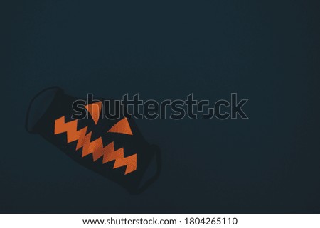 Black protective mask with orange eyes and mouth on a black background.Halloween and covid-19 concept.Copy space for text, top view