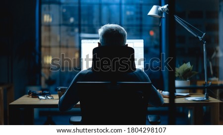 Back view Shot of the Businessman Sitting at His Desk Using Desktop Computer. Stylish Office Studio with Dimmed Light and Big Cityscape Window View Royalty-Free Stock Photo #1804298107