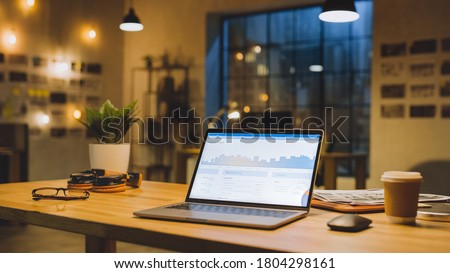 Laptop on the Desk in the Office Shows Company Growth Data with Graphs, Charts, Software UI. In the Background Stylish Modern Office Studio in the Evening with Big Cityscape Window