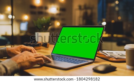 Close-up On the Hands of the Male Specialist Works on a Laptop Computer with Mock-up Green Screen. In the Background Evening in the Stylish Studio Office