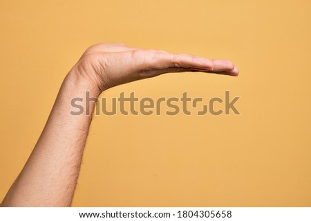 Hand of caucasian young man showing fingers over isolated yellow background with flat palm presenting product, offer and giving gesture, blank copy space