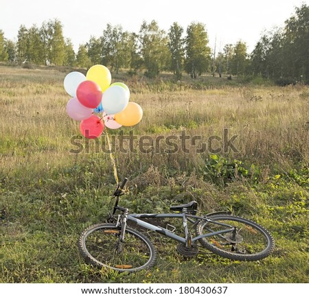 Image of bicycle with colorful balloons lie on fresh green grass on trees and sky background 