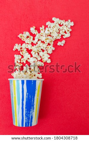Spilled popcorn from a paper Cup on a red background, top view, copy space, vertical photo