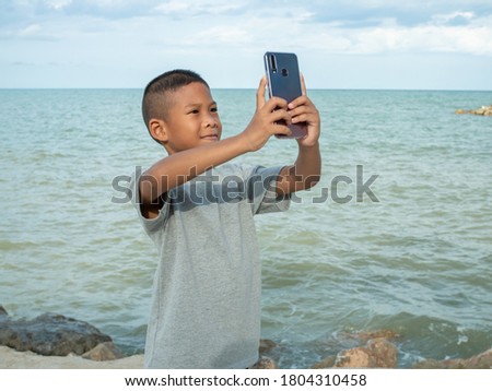 A boy using a phone to take a selfie on a sea background.