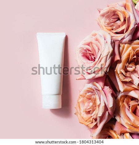 Top view of mockup of white squeeze bottle plastic tube and pink golden roses on a powdery pink background. Bottle for branding and label. Luxury cosmetic. Copy space, Flower flatlay, square photo