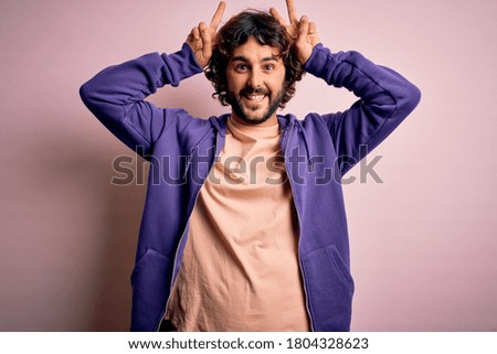 Young handsome sporty man with beard wearing casual sweatshirt over pink background Posing funny and crazy with fingers on head as bunny ears, smiling cheerful