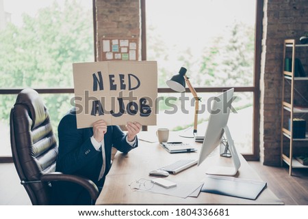 Profile photo of negative laid off office worker sitting holding placard showing his need for new job last working day workplace hiding face shame to be fired bad mood indoors