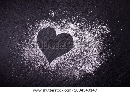 a sprinkle of powdered sugar forms a heart on the black slate stone Royalty-Free Stock Photo #1804343149