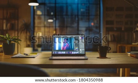 Shot of a Laptop Computer in the Modern Office Showing Photo Editing Software. In the Background Warm Evening Lighting and Open Space Studio with City Window View