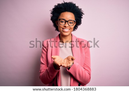 Young beautiful African American afro businesswoman with curly hair wearing pink jacket Smiling with hands palms together receiving or giving gesture. Hold and protection