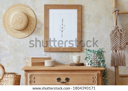 Stylish boho interior of living room with brown mock up poster frame, elegant accessories, flowers, ladder, wooden shelf and hanging rattan hut. Minimalistic concept of home decor. Template.