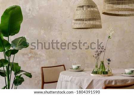 Stylish and elegant dining room interior with diner table, design chairs, rattan pendant lamps, beautiful flowers in vases, furniture, decoration and elegant personal accessories in cozy home decor. Royalty-Free Stock Photo #1804391590