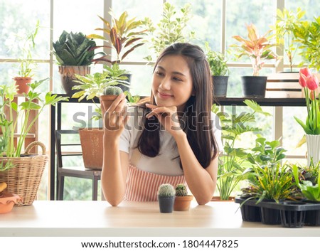 Portrait young woman, beautiful, cute. Asians wear white shirts with long black hair. Smile with bright smile look small trees (cantus) in hand and on wooden table in gardening room happily and relax