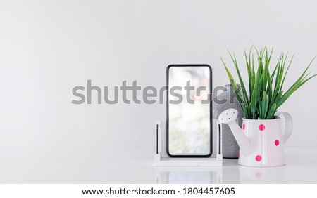 Mockup blank screen smartphone and houseplant on white table, copy space, blank screen for graphic design.