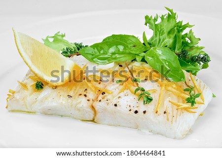 Cooked white fish fillet with black pepper, lemon slices, fresh arugula and basil leaves close-up isolated on white