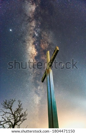 The tree, the cross and the milky Way galaxy. Image contain soft focus and blur due to long expose and wide aperture. Image also contain noise and grains due to high ISO.