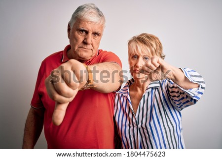 Senior beautiful couple standing together over isolated white background looking unhappy and angry showing rejection and negative with thumbs down gesture. Bad expression.