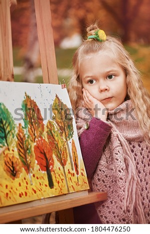 pensive portrait of a child. little girl artist on the background of painted paintings in autumn in the park