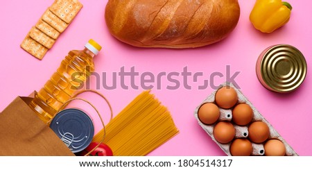 Set of products on pink isolated background. Bread, chicken eggs, pasta, yellow fresh pepper, tomatoes, sunflower oil, canned food, cookies, in paper bag