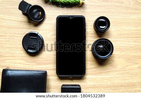 Smartphone and lens on tbe table with wood background.