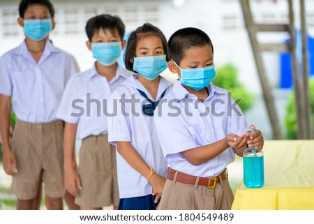 Elementary school students wearing hygienic mask to prevent the outbreak of Covid 19 spraying classmate's hands at school after covid-19 quarantine and lockdown.