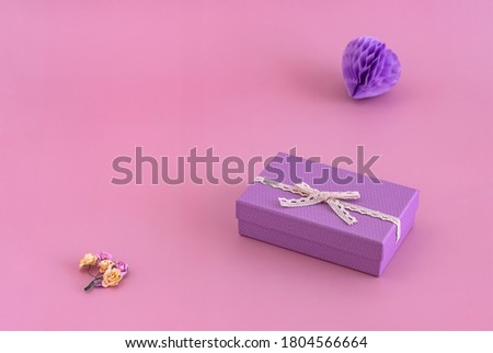 purple gift box, paper toy in the shape of a heart and small dry flowers on a pink background
