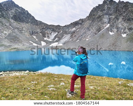 Young active woman with photographic camera taking photo at blue water background. Imeretinsky Lake Bush in Russia