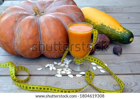Still life with vegetables and diet pumpkin juice for weight loss. A huge pumpkin, zucchini, glass, seeds and a centimeter ribbon.