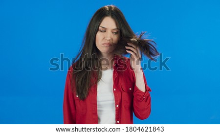 Young woman unhappy with her hair condition.Charming young woman with long brunette hair notices that her hair is in bad condition. Beauty concept.