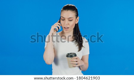 Portrait of a young woman talking on the phone, drinking coffee, smiling, listening, sad, on a blue background. 