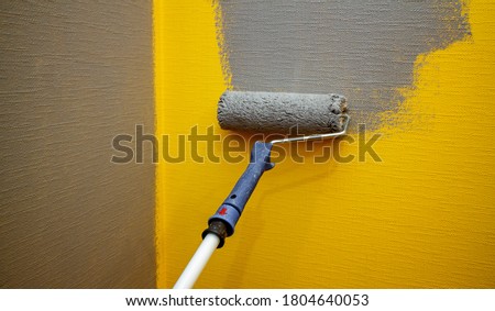 Close up roller with gray paint for painting walls. Repairs. Yellow wall. Background. Screensaver for the site. High quality photo. Art noise.