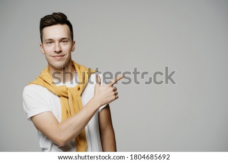 a young man of Caucasian appearance points his finger at your company logo. stylish brunette hairstyle. white t-shirt and yellow jacket on the shoulders. grey background photo Studio
