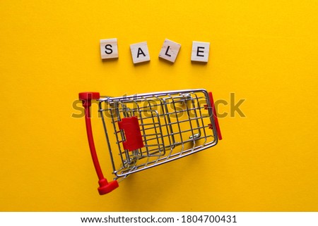 Word SALE made from wooden letters and grocery cart on yellow background. Shopping, discounts, season sales and black friday concept. For business. Top view, flat lay, close-up